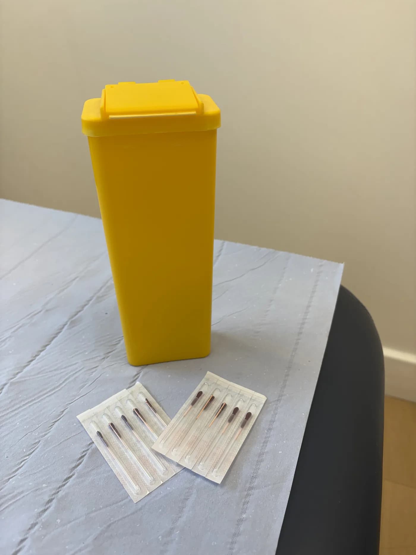 Single-use acupuncture needles and a sharps bin laid out on the treatment table at Atlas Osteopathy.